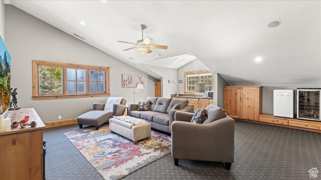 Carpeted living room featuring vaulted ceiling, ceiling fan, and a healthy amount of sunlight