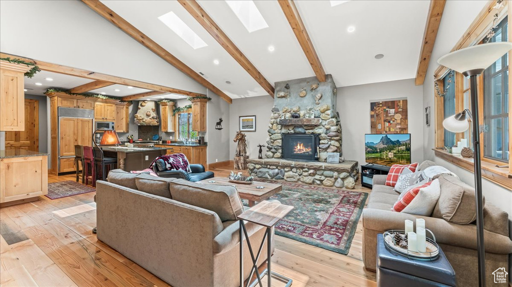 Living room featuring high vaulted ceiling, beam ceiling, light wood-type flooring, a skylight, and a fireplace