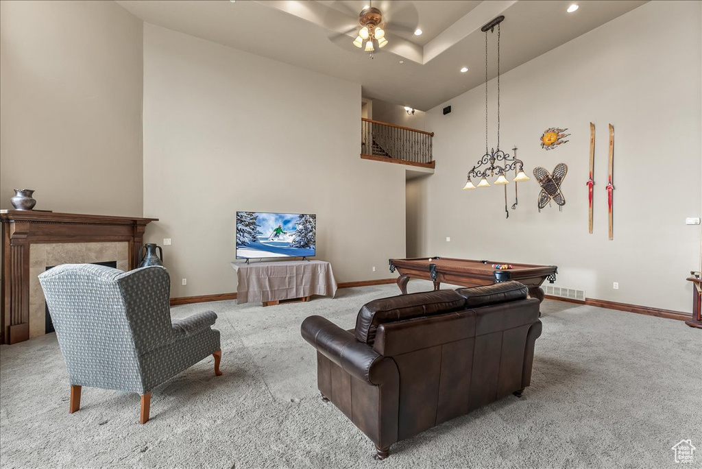 Living room featuring ceiling fan, light colored carpet, a tiled fireplace, a towering ceiling, and pool table