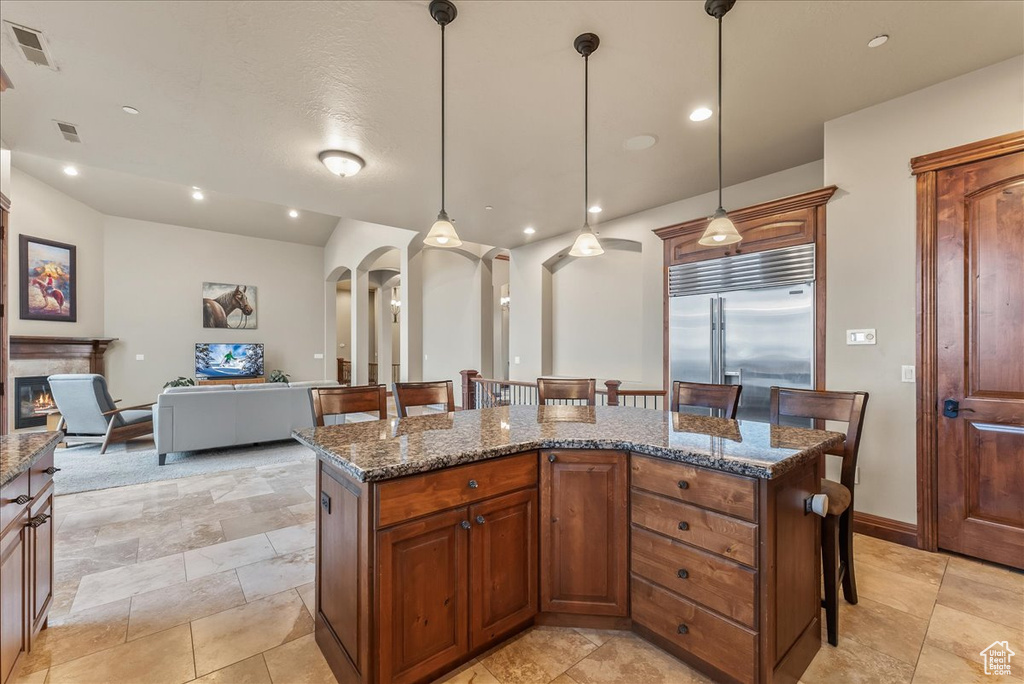 Kitchen with decorative light fixtures, built in refrigerator, dark stone countertops, and a breakfast bar area
