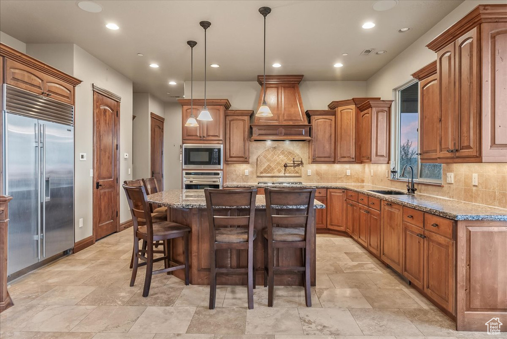 Kitchen with a kitchen breakfast bar, stone counters, built in appliances, custom range hood, and a kitchen island