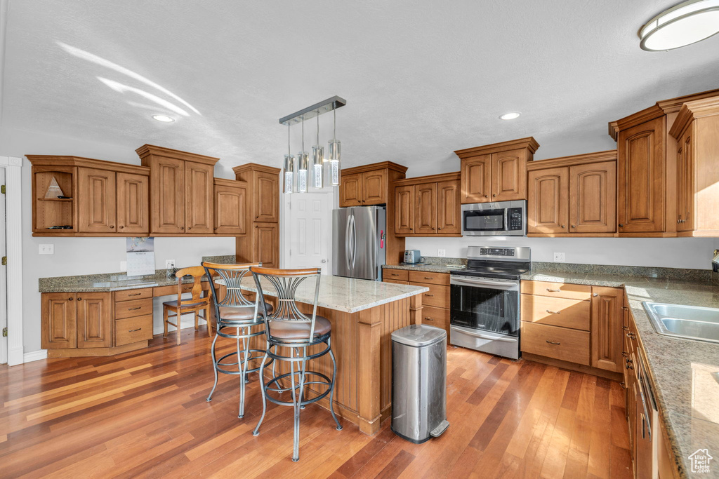 Kitchen with a center island, a breakfast bar, pendant lighting, light hardwood / wood-style floors, and appliances with stainless steel finishes