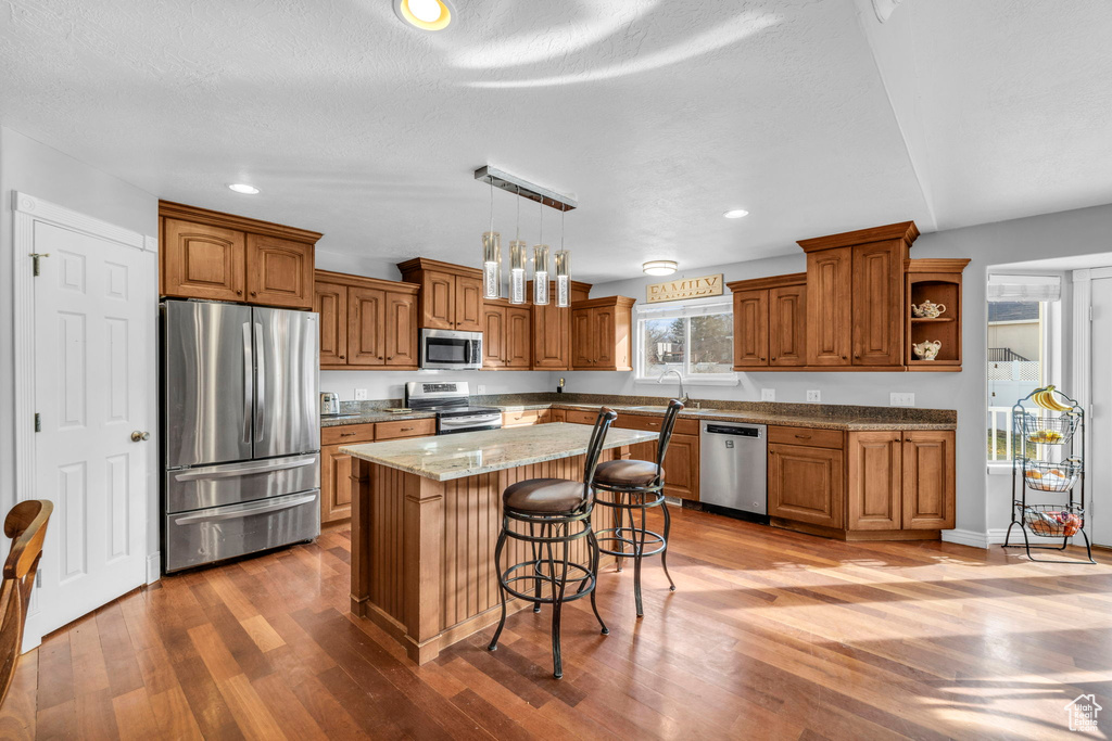 Kitchen featuring appliances with stainless steel finishes, decorative light fixtures, a center island, and hardwood / wood-style floors