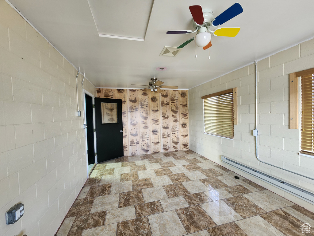 Tiled empty room featuring a baseboard heating unit and ceiling fan