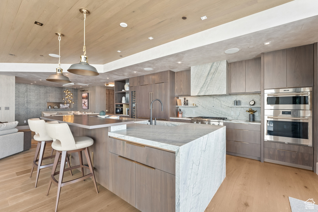Kitchen featuring tasteful backsplash, appliances with stainless steel finishes, a large island, light wood-type flooring, and a kitchen bar
