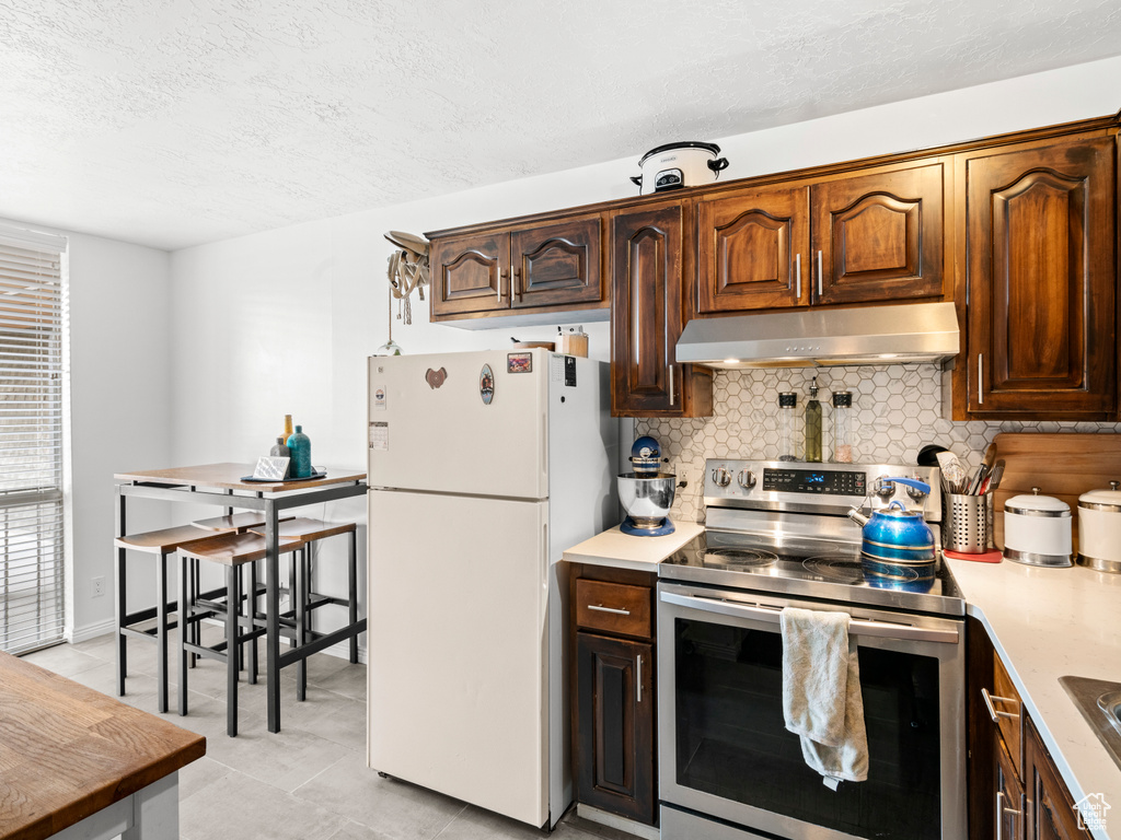 Kitchen with stainless steel range with electric stovetop, white fridge, tasteful backsplash, and light tile flooring