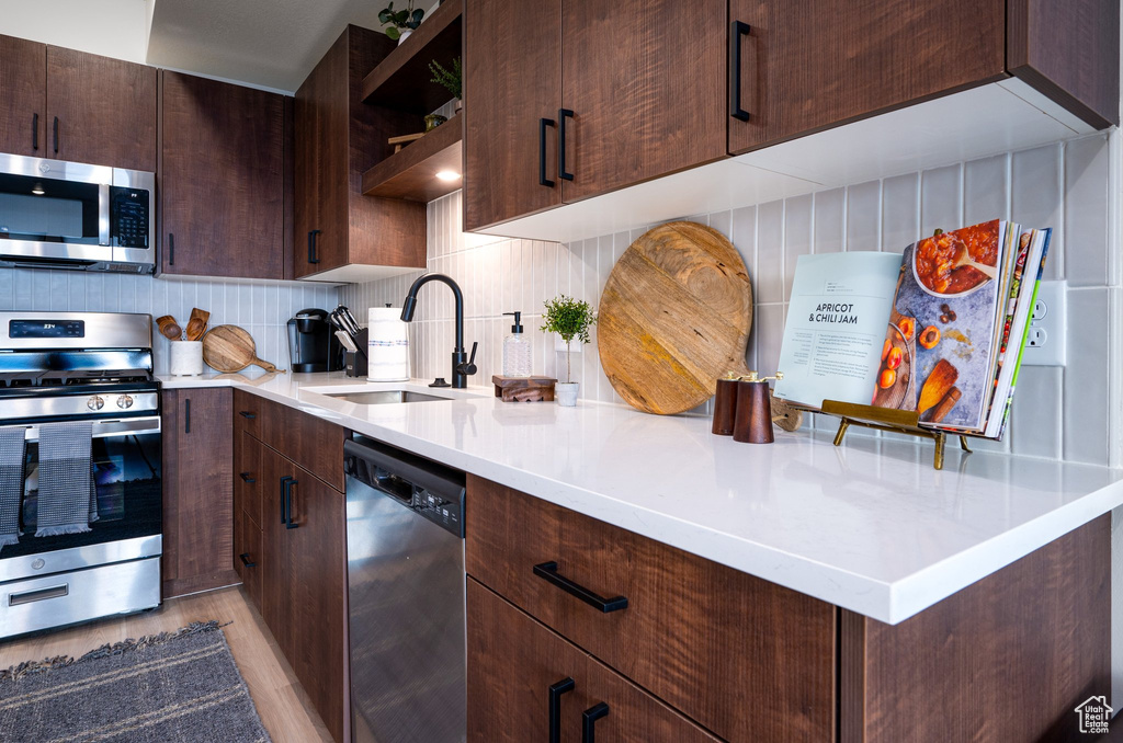 Kitchen featuring sink, tasteful backsplash, dark brown cabinetry, appliances with stainless steel finishes, and light hardwood / wood-style flooring
