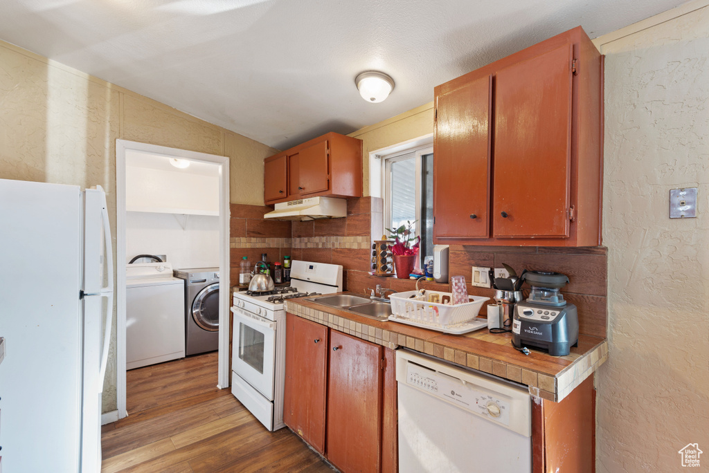 Kitchen with washer and dryer, white appliances, lofted ceiling, and hardwood / wood-style floors
