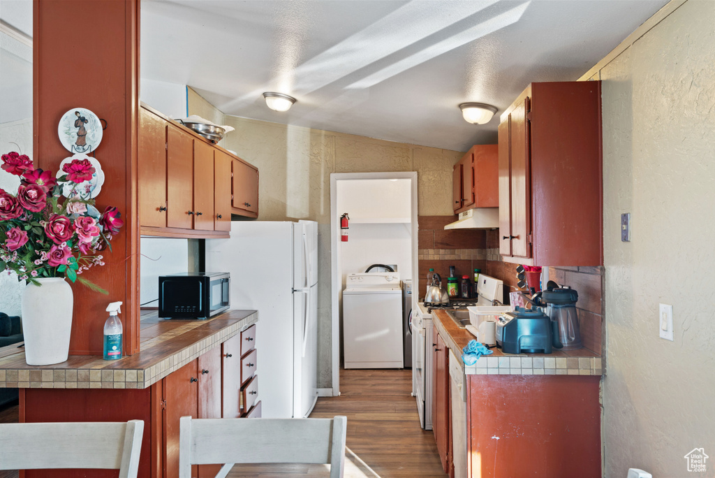 Kitchen featuring tasteful backsplash, vaulted ceiling, dark hardwood / wood-style floors, white appliances, and washer / clothes dryer