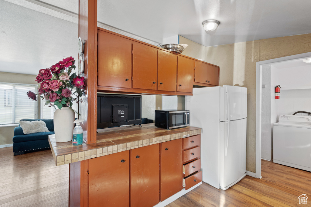 Kitchen with washer / clothes dryer, white refrigerator, light hardwood / wood-style floors, and tile counters