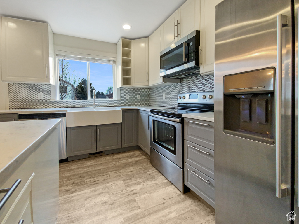 Kitchen featuring sink, appliances with stainless steel finishes, light wood-type flooring, gray cabinetry, and backsplash