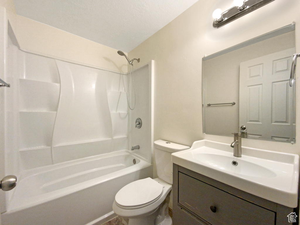 Full bathroom featuring toilet, vanity with extensive cabinet space, a textured ceiling, and bathtub / shower combination