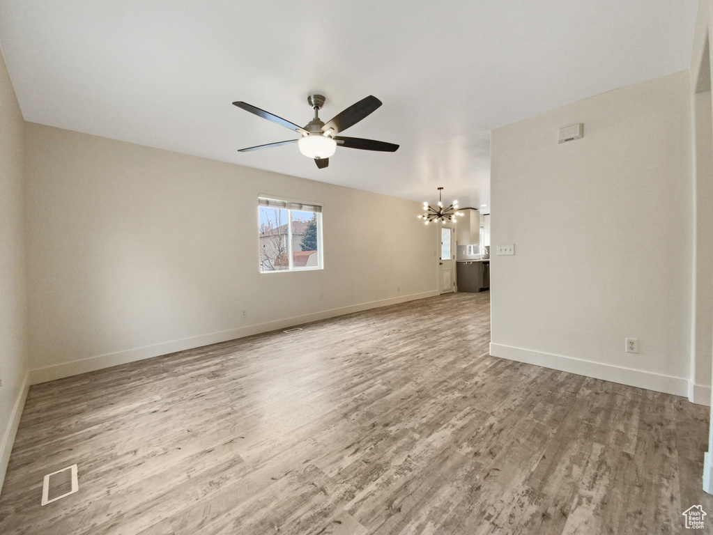 Unfurnished room with ceiling fan with notable chandelier and light wood-type flooring