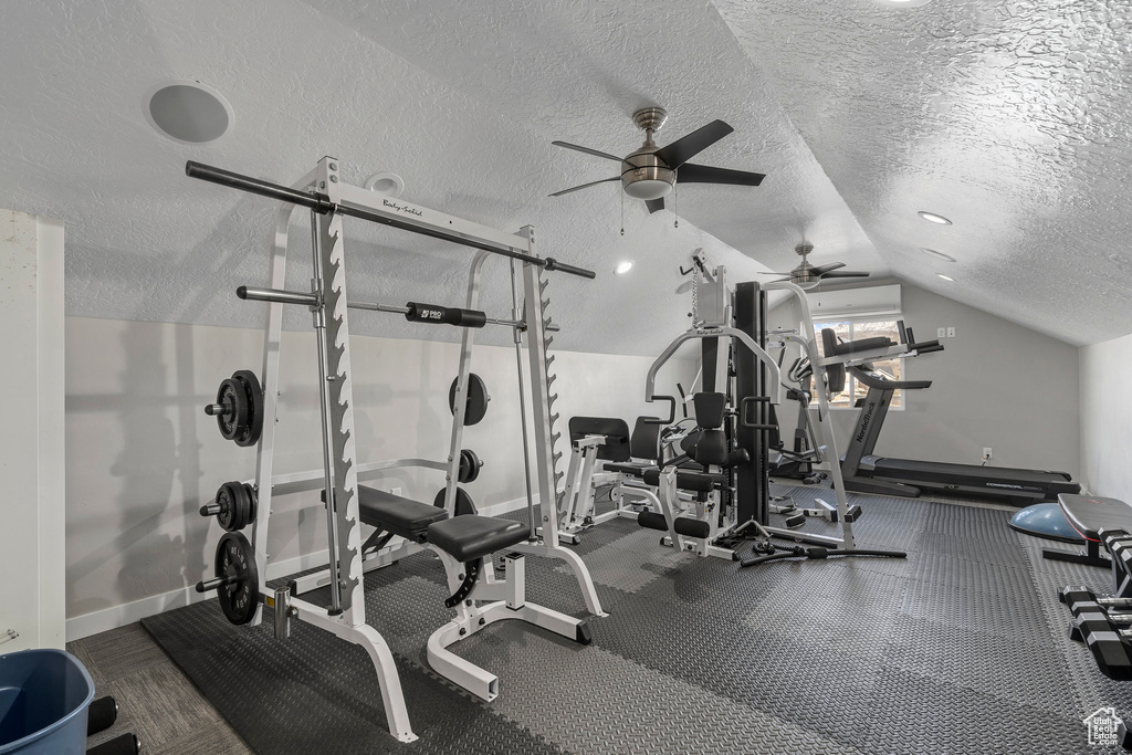 Exercise area with dark carpet, a textured ceiling, vaulted ceiling, and ceiling fan