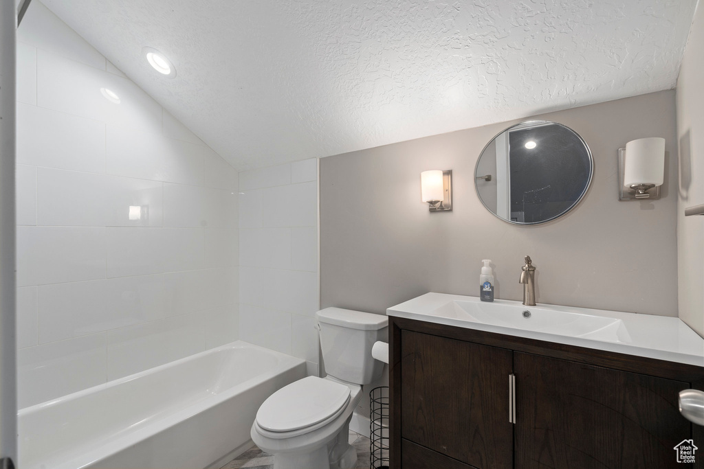 Full bathroom with lofted ceiling, a textured ceiling, tub / shower combination, toilet, and vanity