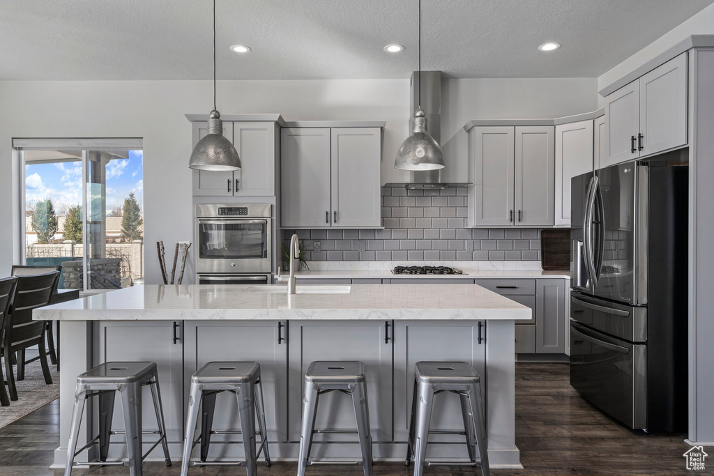 Kitchen featuring gray cabinets, wall chimney range hood, hanging light fixtures, dark hardwood / wood-style flooring, and stainless steel appliances