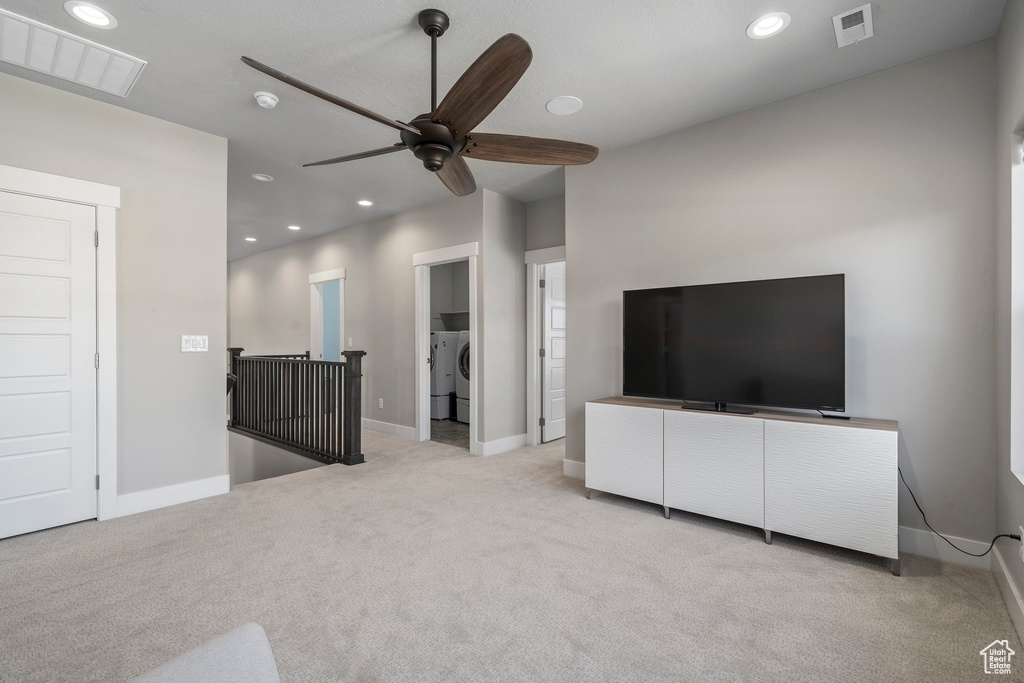 Unfurnished living room with light colored carpet, independent washer and dryer, and ceiling fan