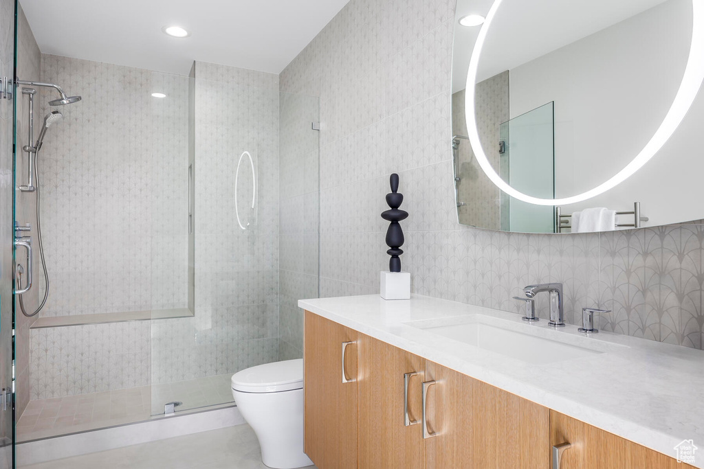 Bathroom featuring tasteful backsplash, tile walls, a shower with shower door, vanity, and toilet