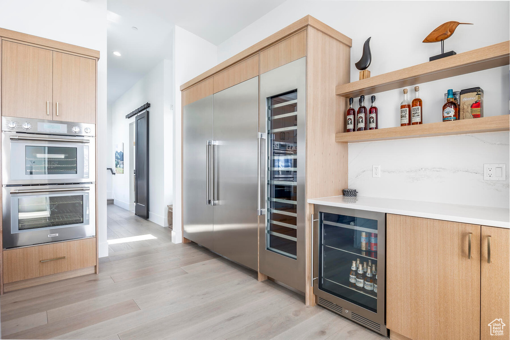 Kitchen featuring light brown cabinets, double oven, light hardwood / wood-style floors, and beverage cooler