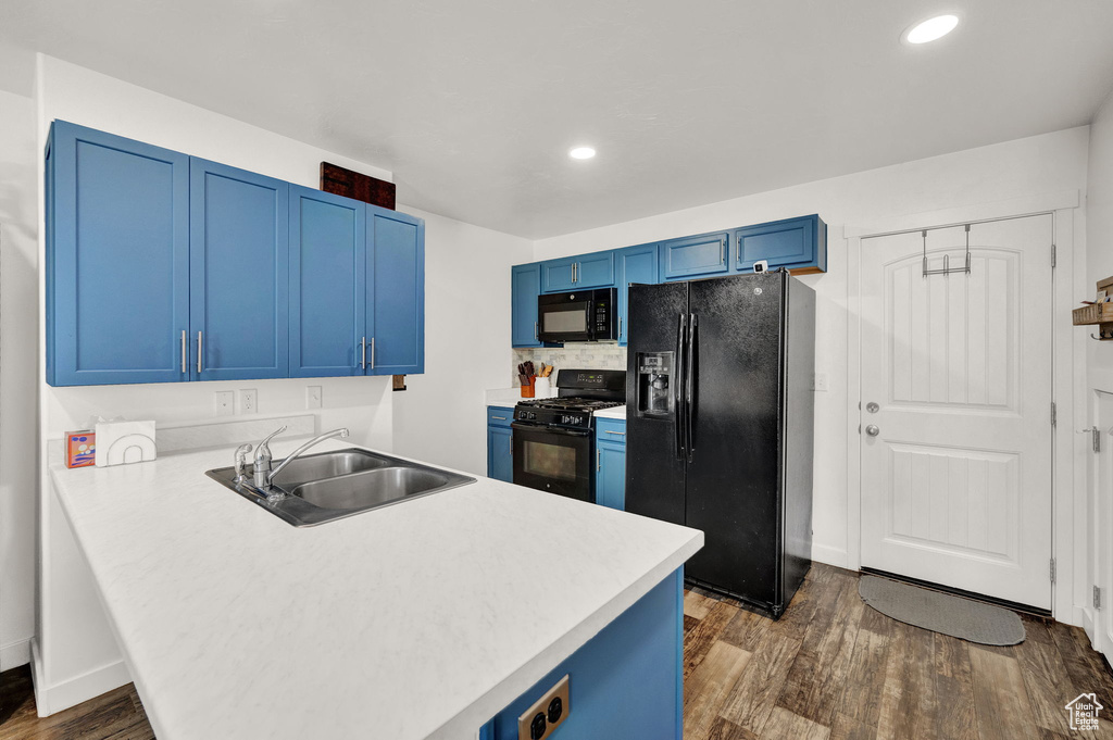 Kitchen with black appliances, dark hardwood / wood-style floors, blue cabinetry, and sink