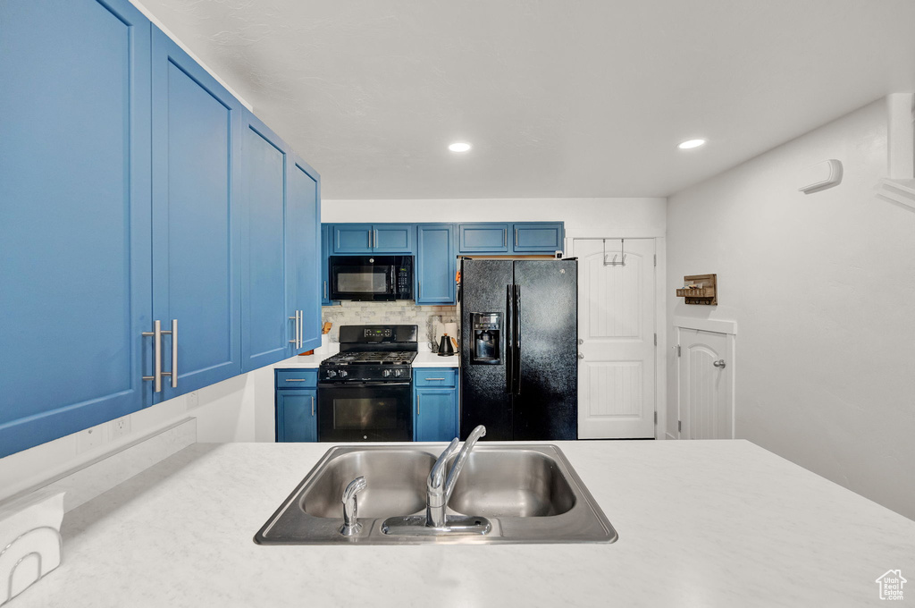Kitchen with black appliances, backsplash, sink, and blue cabinetry