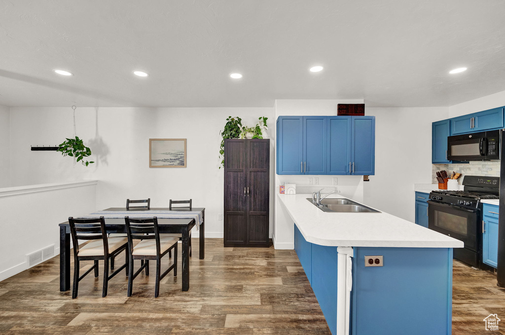 Kitchen with tasteful backsplash, blue cabinetry, dark wood-type flooring, sink, and black appliances