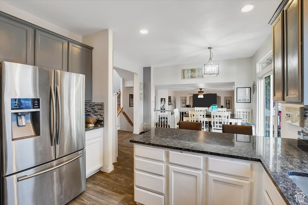 Kitchen with stainless steel fridge, ceiling fan, dark hardwood / wood-style floors, dark stone counters, and pendant lighting