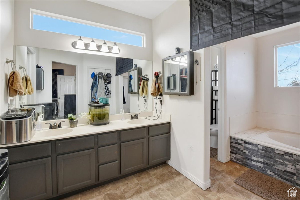 Bathroom featuring dual sinks, plenty of natural light, tile floors, oversized vanity, and tiled tub