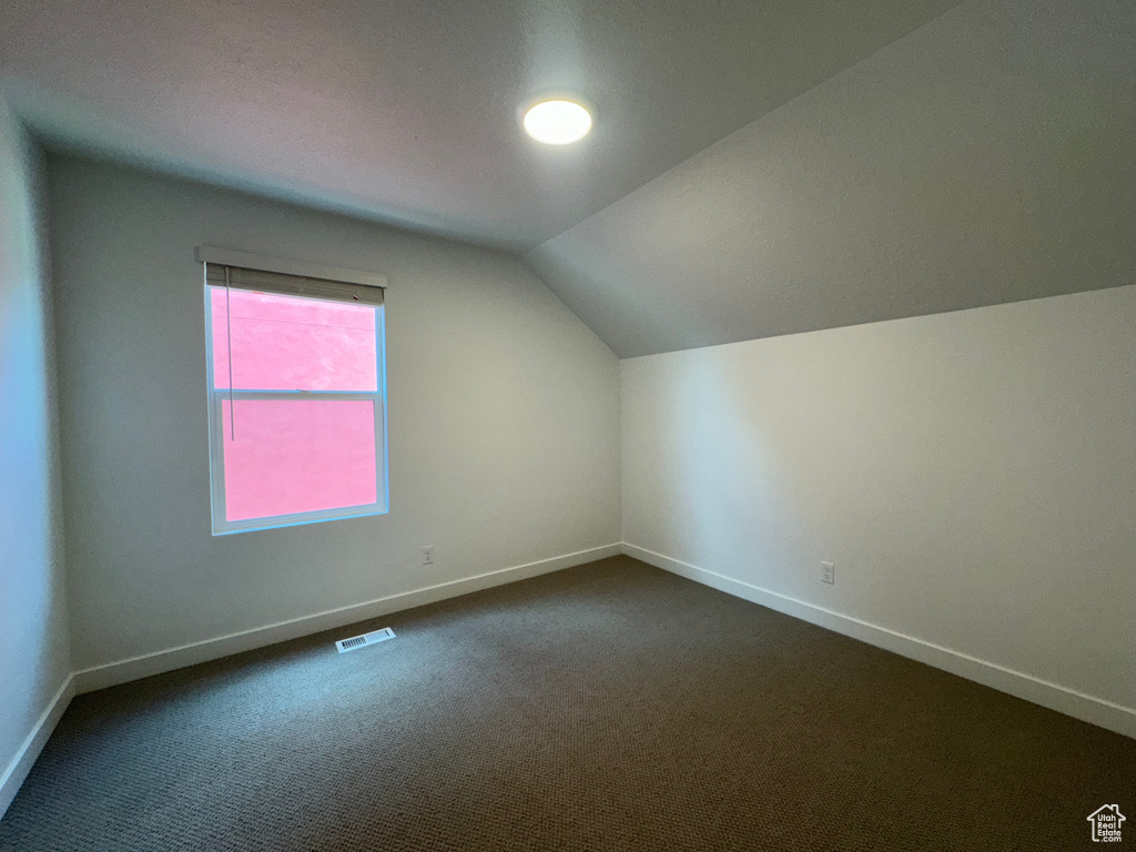 Additional living space featuring vaulted ceiling and dark colored carpet