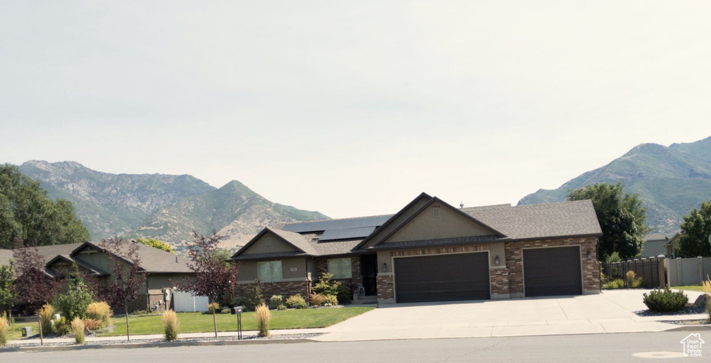 View of front of home featuring solar panels, a mountain view, a garage, and a front yard