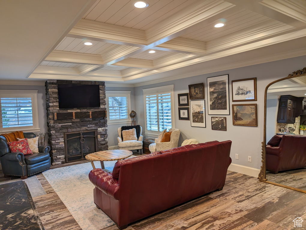 Living room featuring a stone fireplace, coffered ceiling, beamed ceiling, light wood-type flooring, and crown molding