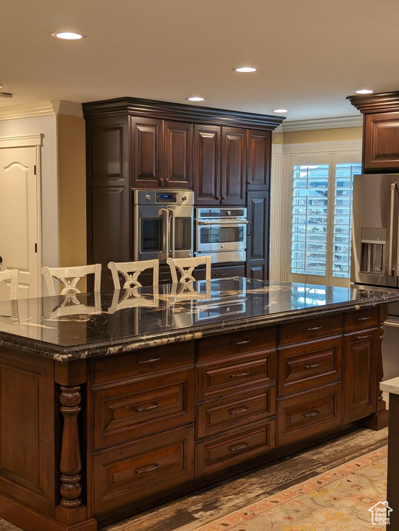 Kitchen with appliances with stainless steel finishes, crown molding, and dark stone counters