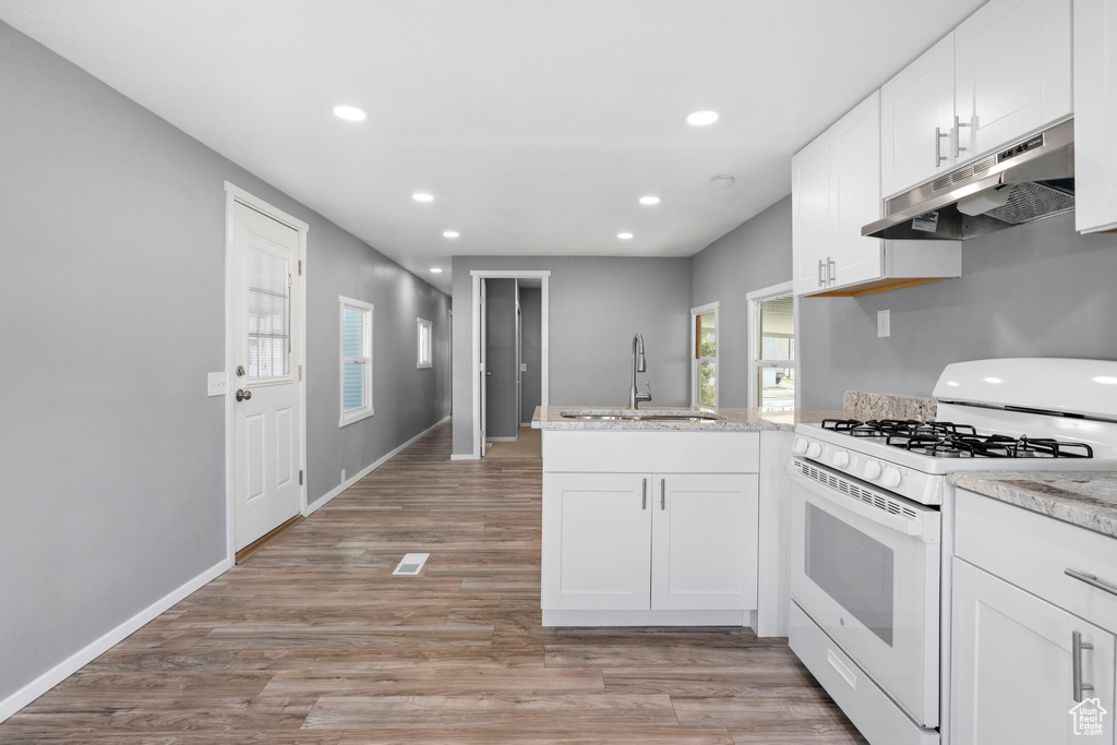 Kitchen with white range with gas cooktop, sink, light wood-type flooring, white cabinetry, and kitchen peninsula