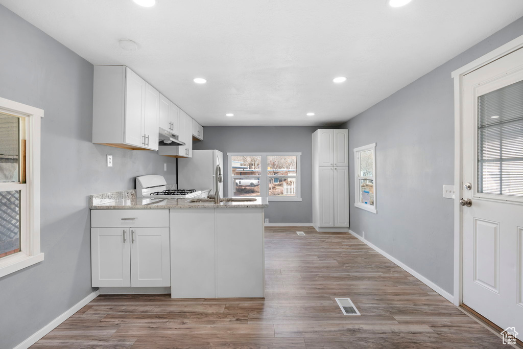 Kitchen featuring white cabinetry, light hardwood / wood-style flooring, kitchen peninsula, and range
