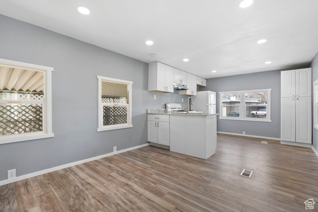 Kitchen with white cabinets, light hardwood / wood-style floors, kitchen peninsula, white refrigerator, and light stone countertops