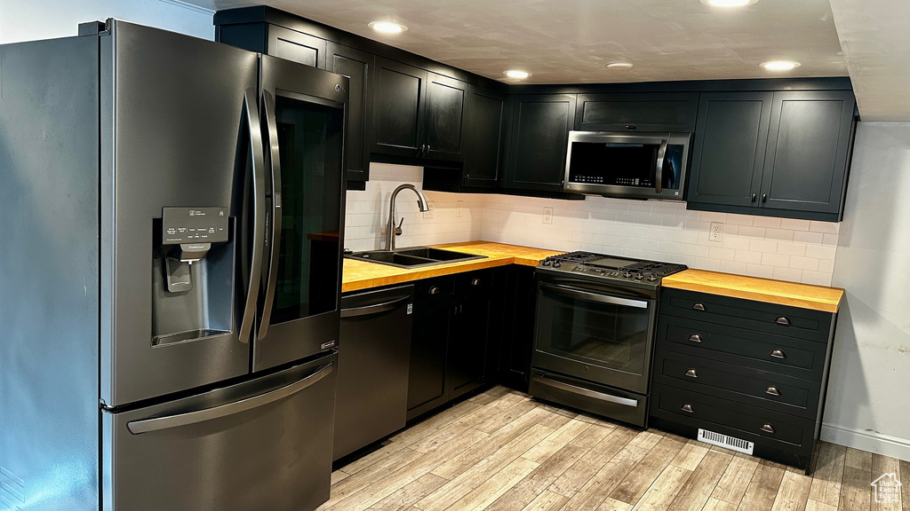 Kitchen featuring sink, light hardwood / wood-style floors, butcher block countertops, backsplash, and black appliances