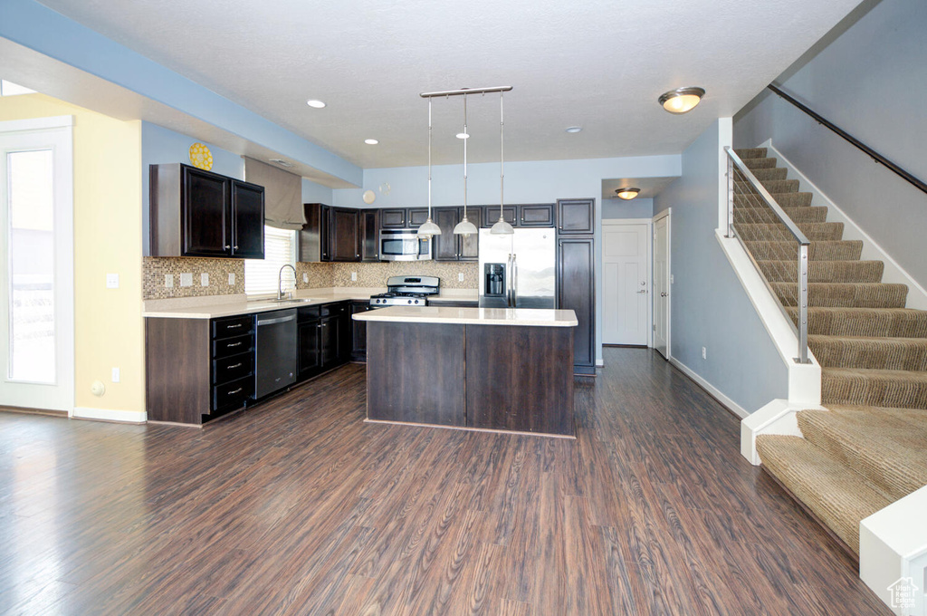 Kitchen featuring stainless steel appliances, a center island, hanging light fixtures, and dark wood-type flooring