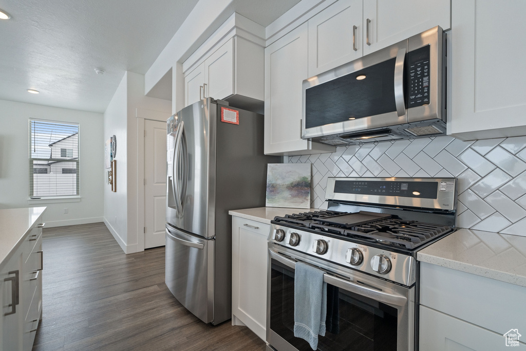 Kitchen featuring dark hardwood / wood-style floors, stainless steel appliances, white cabinets, and tasteful backsplash