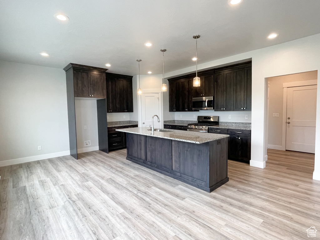 Kitchen with appliances with stainless steel finishes, pendant lighting, a kitchen island with sink, and light hardwood / wood-style floors