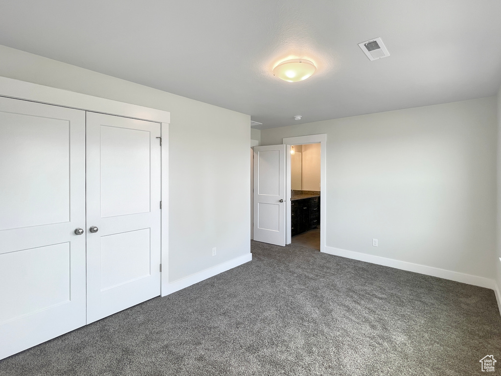 Unfurnished bedroom featuring dark colored carpet, a closet, and ensuite bathroom