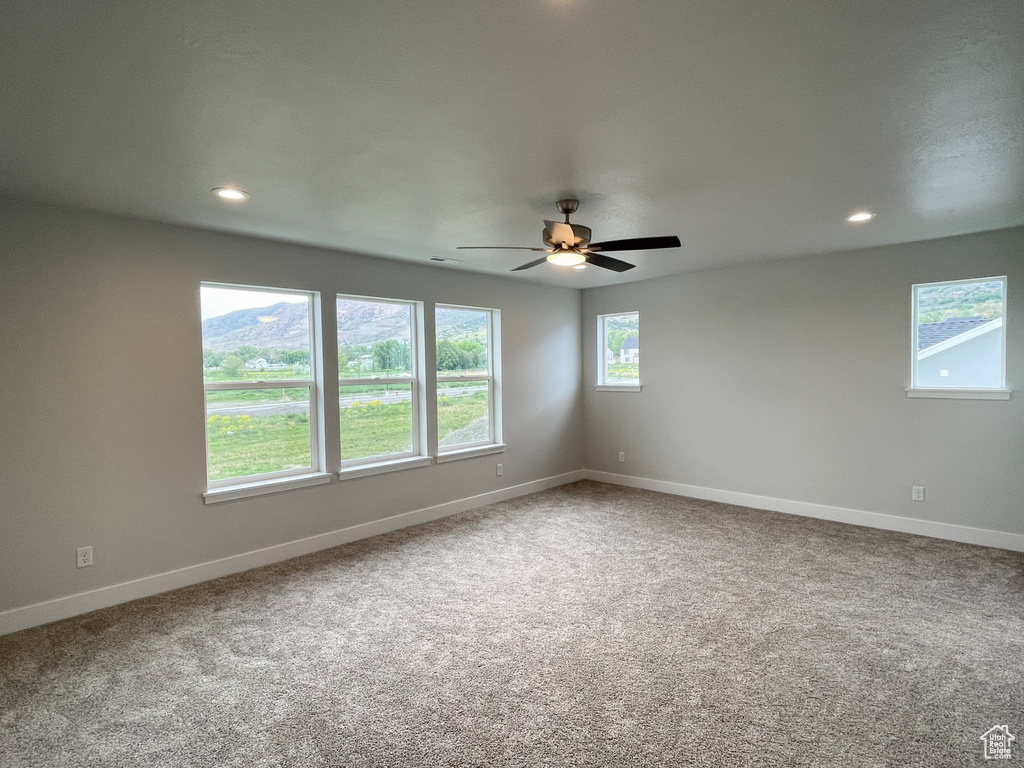 Spare room featuring a wealth of natural light, carpet flooring, and ceiling fan