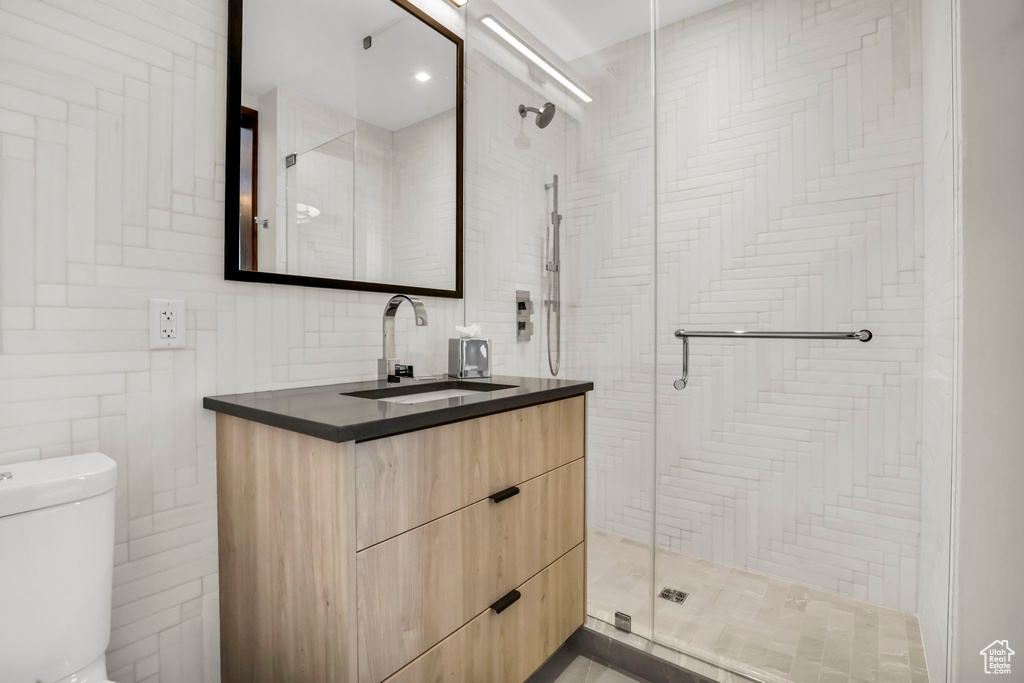 Bathroom featuring tile walls, toilet, vanity, and walk in shower