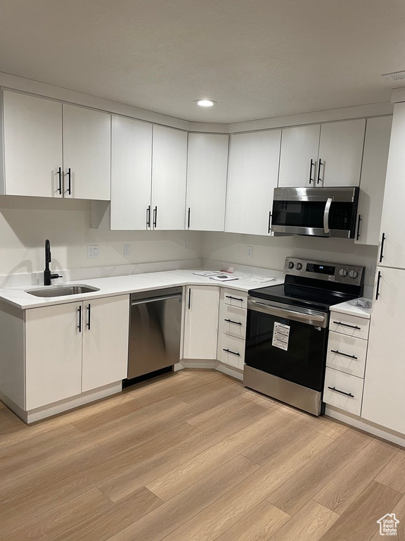 Kitchen featuring appliances with stainless steel finishes, light hardwood / wood-style flooring, white cabinets, and sink