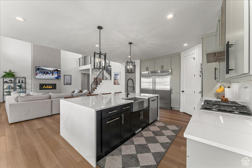 Kitchen with sink, pendant lighting, light hardwood / wood-style floors, a center island with sink, and appliances with stainless steel finishes