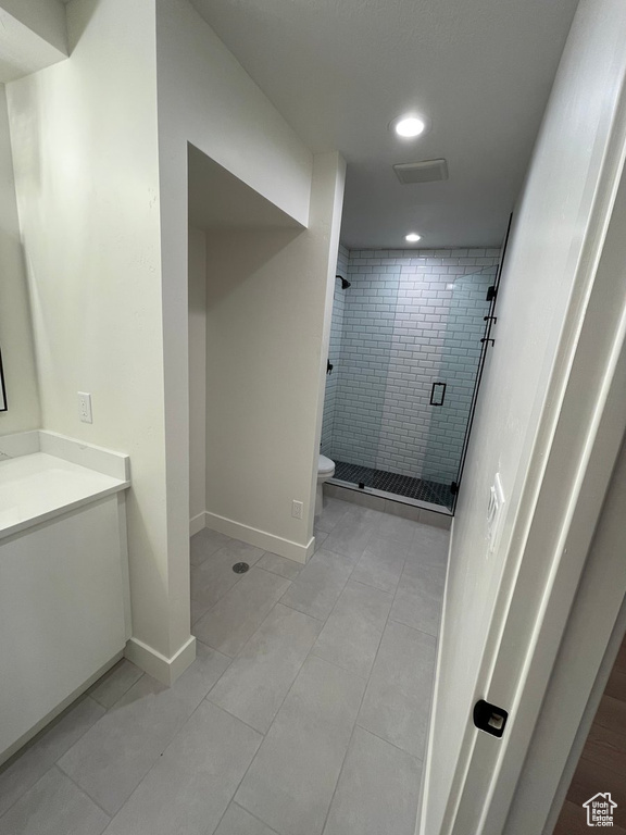 Bathroom featuring a shower with door, tile flooring, toilet, and vanity