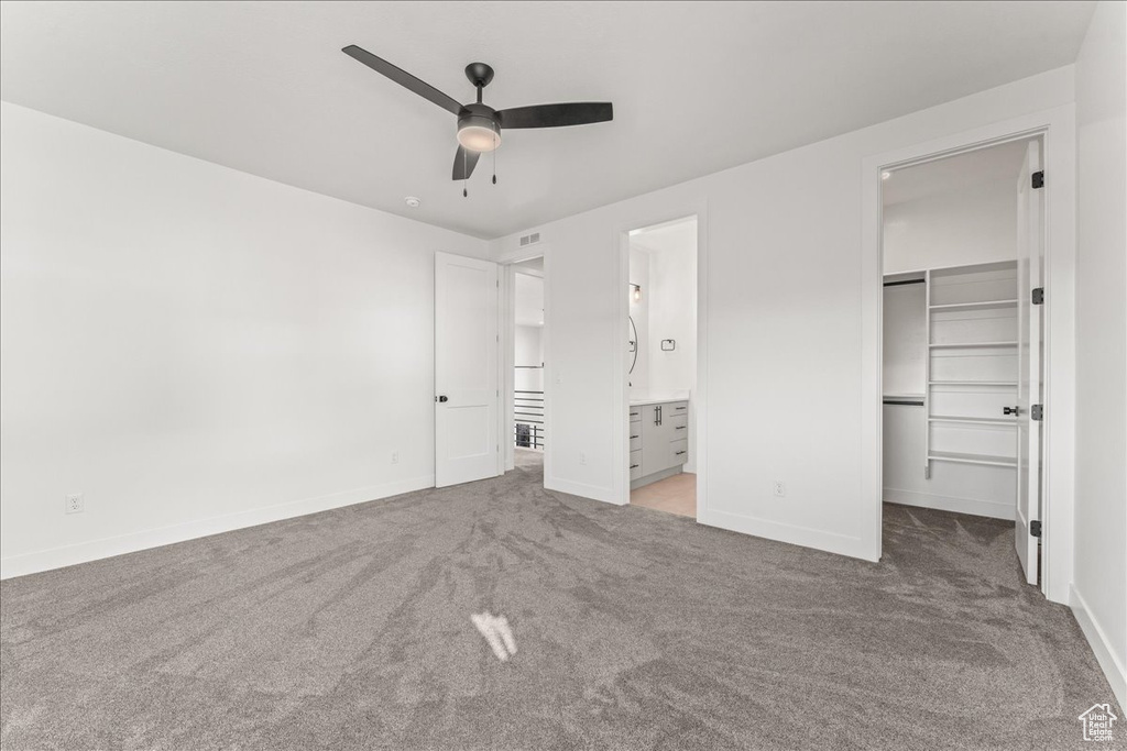 Unfurnished bedroom featuring carpet floors, a closet, ensuite bath, ceiling fan, and a spacious closet