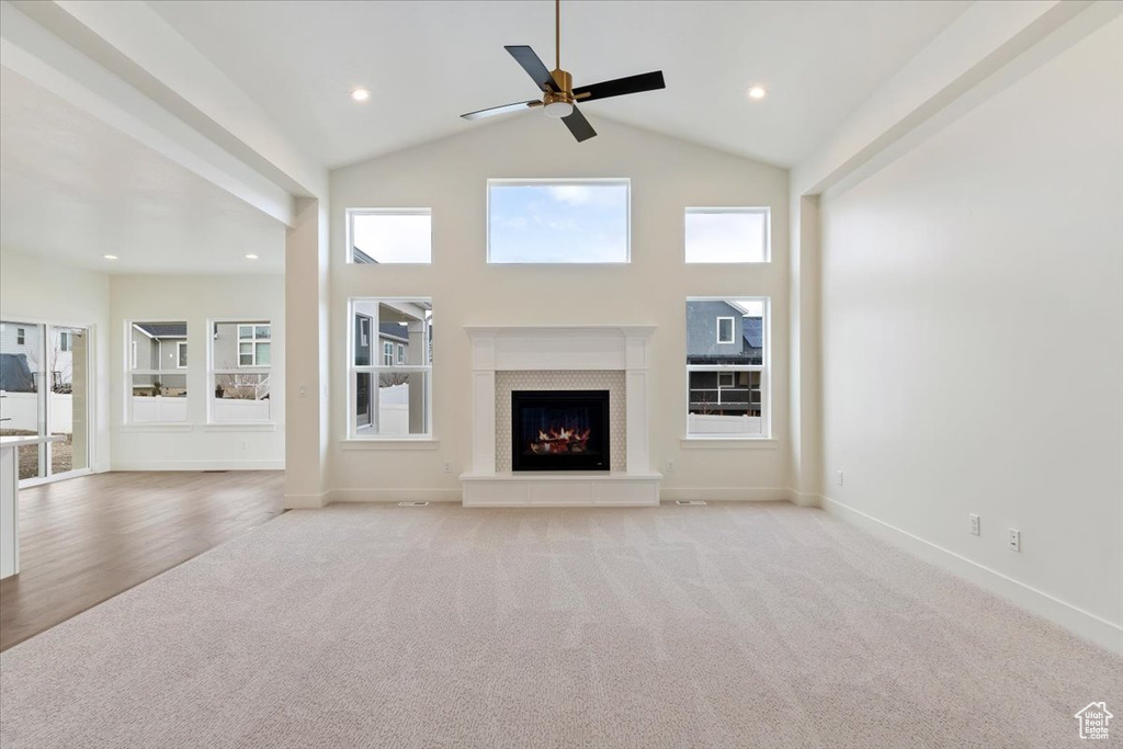 Unfurnished living room with light carpet, high vaulted ceiling, and ceiling fan