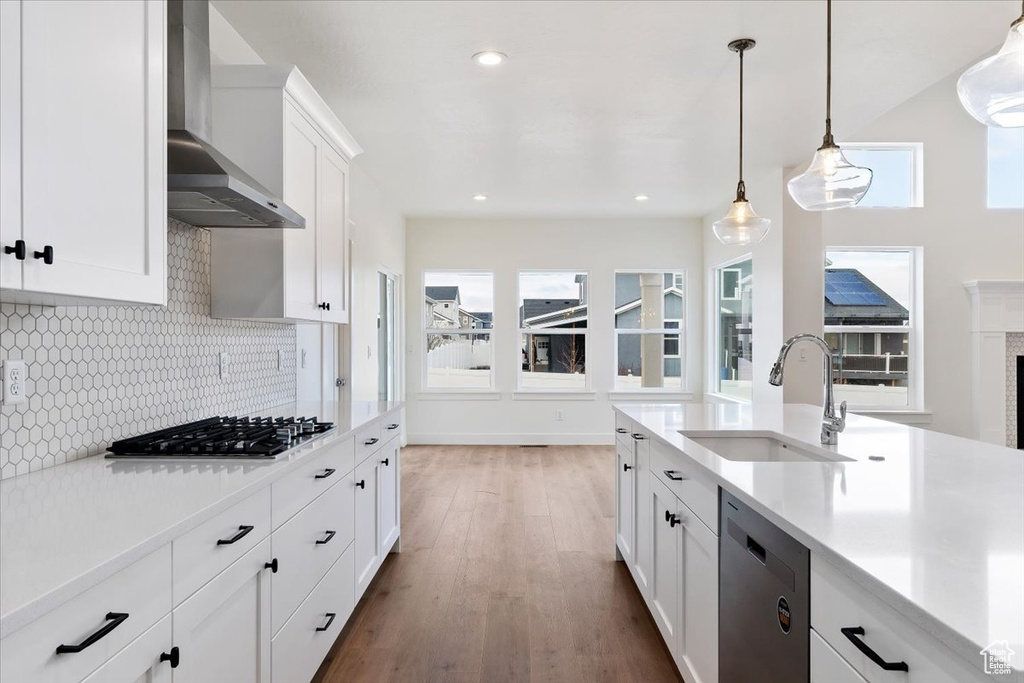 Kitchen with sink, wall chimney exhaust hood, hardwood / wood-style flooring, backsplash, and pendant lighting