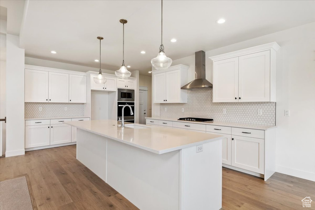 Kitchen with white cabinets, wall chimney range hood, pendant lighting, and backsplash