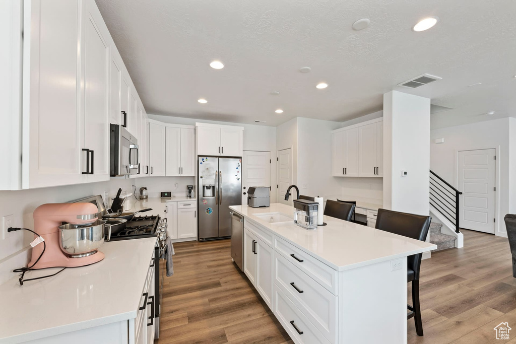 Kitchen featuring appliances with stainless steel finishes, white cabinets, a kitchen island with sink, a breakfast bar area, and light hardwood / wood-style flooring